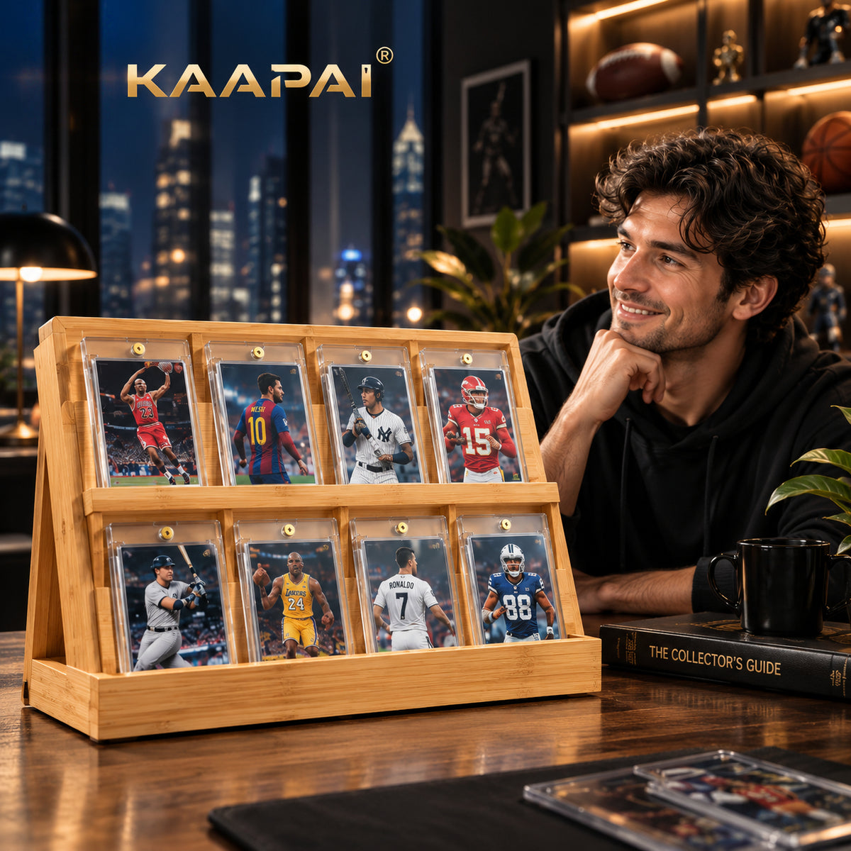 A wooden display stand holding eight framed sports trading cards, shown on a table beside a man in a dark hoodie in a warmly lit room. The brand name KAAPAI appears at the top left.
