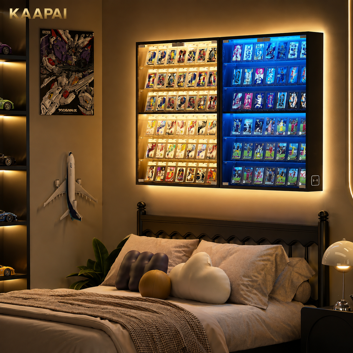 A wall-mounted KAAPAI LED display cabinet with illuminated card slots, shown installed above a bed in a modern bedroom. The cabinet has two columns of lighting: warm yellow on the left and cool blue on the right, showcasing many small collectible cards or figures.