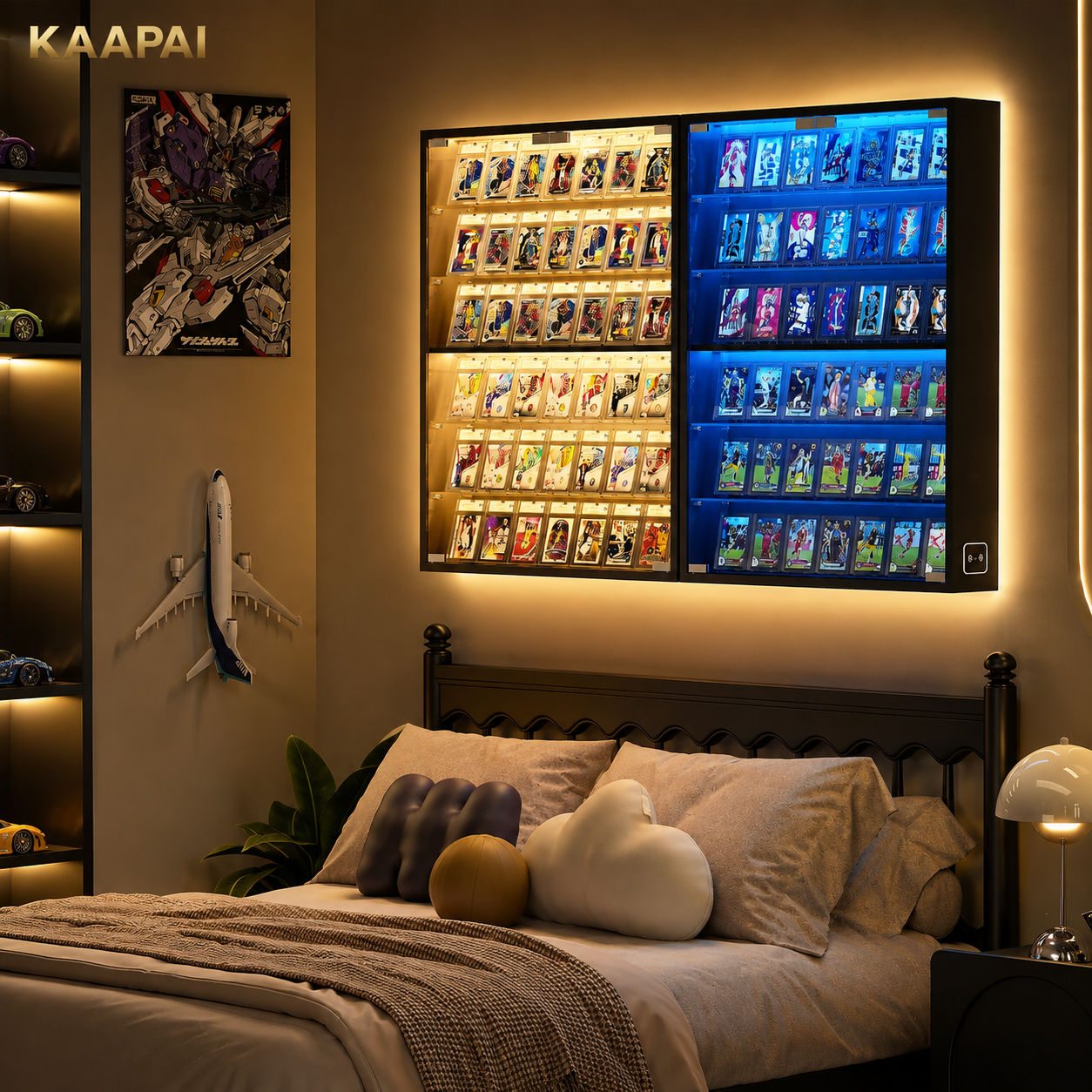 A wall-mounted KAAPAI LED display cabinet with illuminated card slots, shown installed above a bed in a modern bedroom. The cabinet has two columns of lighting: warm yellow on the left and cool blue on the right, showcasing many small collectible cards or figures.